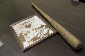 A vintage photo of baseball player Babe Ruth sits on a table next to a wooden practice bat he used to use.