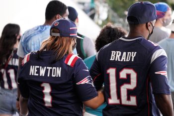 Patriots fans wearing Tom Brady and Cam Newton jerseys walk together during a game at Hard Rock Stadium.