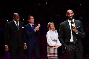 Los Angeles Lakers legend Kobe Bryant addressing a crowd with team owner Jeanie Buss behind him.