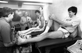 Boston Celtics trainer Ray Melchiorre, left, tapes Kevin McHale's ankles, right, as Bill Walton, center, looks on in Boston, May 14, 1987.